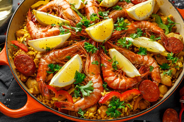 Traditional paella in the fry pan with chicken, prawns, spicy chorizo, lemon and glass of white wine.