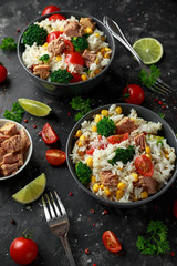 Fresh Tuna rice salad with sweet corn, cherry tomatoes, broccoli, parsley and lime in black bowl