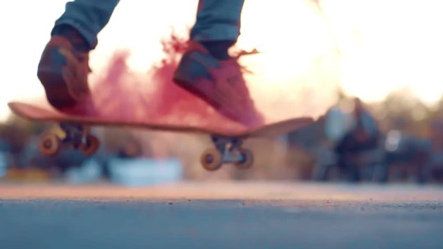 Skateboarder does extreme flip trick with colored powder in slow motion. paints fly in different directions. concept of fun and sports