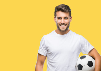 Young handsome man holding soccer football ball over isolated background with a happy face standing...