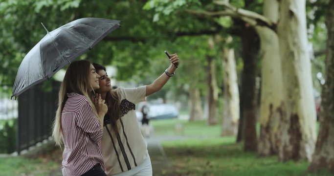 Rain day two girls taking selfies in the middle of street under the umbrella. 4k