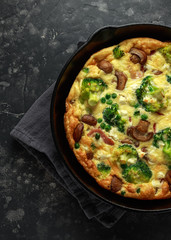 Homemade Frittata with mushrooms, broccoli, feta cheese, green peas and bacon on cast iron skillet