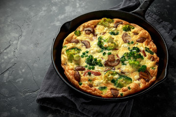 Homemade Frittata with mushrooms, broccoli, feta cheese, green peas and bacon on cast iron skillet