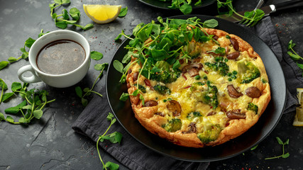 Homemade Frittata with mushrooms, broccoli, feta cheese, green peas and bacon on black plate