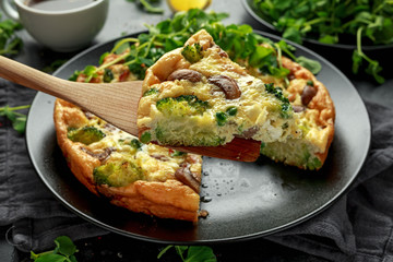 Homemade Frittata with mushrooms, broccoli, feta cheese, green peas and bacon on black plate