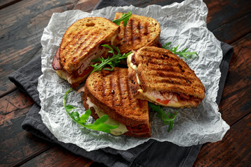 grilled sandwich with turkey, bacon, tomato and cheese on rustic wooden background