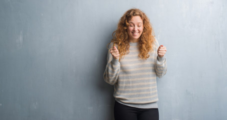 Fototapeta premium Young redhead woman over grey grunge wall excited for success with arms raised celebrating victory smiling. Winner concept.