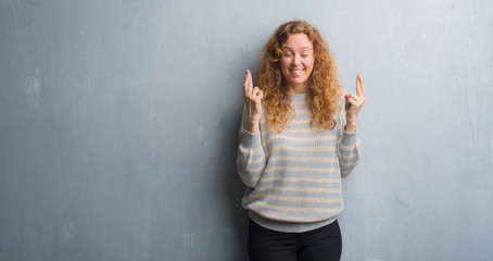 Fototapeta premium Young redhead woman over grey grunge wall smiling crossing fingers with hope and eyes closed. Luck and superstitious concept.