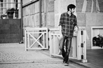 Young indian student man at red checkered shirt and jeans posed at city.