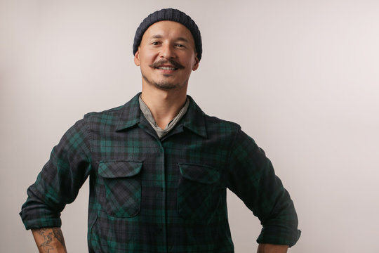 Portrait of kind cheerful smart professional friendly expert handsome handyman wearing knitted hat standing isolated on gray background copyspace