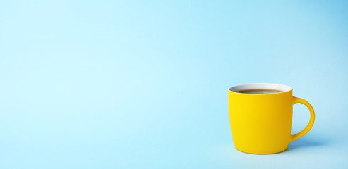 Yellow ceramic cup with hot aromatic coffee on color background