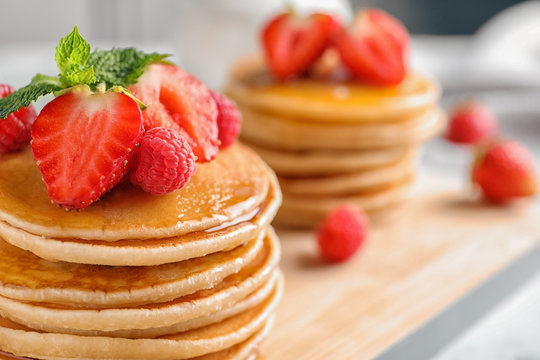 Tasty pancakes with berries and honey on wooden board, closeup