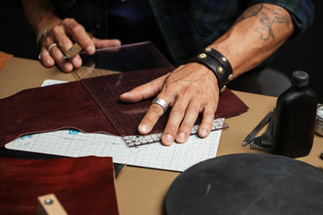 A close-up of a man skinner makes leather pattern with the help of a special knife in the workshop. Leather Craftsman manufactures a custom made pocketbook.