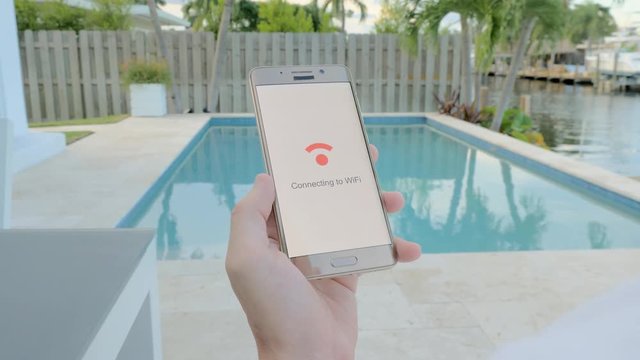 Man on vacation sitting by the pool holding a smartphone that connects to WiFi