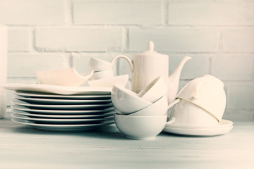 White porcelain  dishware stacked on a wooden table against white brick background. Concept of restaurant, cooking and service.