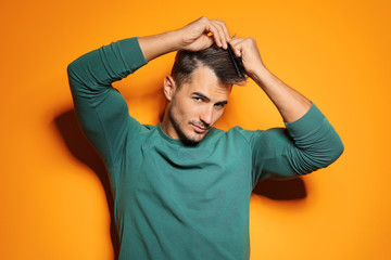 Young man with comb posing on color background. Trendy hairstyle