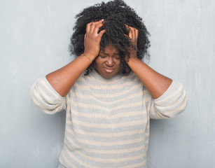 Young african american plus size woman over grey grunge wall wearing a sweater suffering from headache desperate and stressed because pain and migraine. Hands on head.