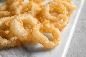 Closeup view of delicious golden breaded and deep fried crispy onion rings on marble board