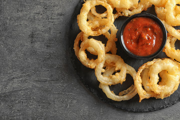 Top view of delicious onion rings and sauce on gray background, closeup. Space for text