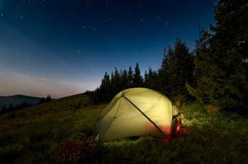 Astrophotography of night camp and starry skies at Carpatian mountains in Ukraine. Green tent on the foreground is highlighted from the inside. Concept of  backpacking travel lifestyle.