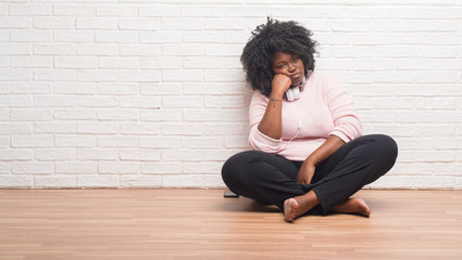 Young african american woman sitting on the floor wearing headphones thinking looking tired and bored with depression problems with crossed arms.