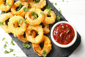 Homemade crunchy fried onion rings with tomato sauce on wooden table, top view