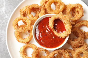 Homemade crunchy fried onion rings with sauce on color table, top view