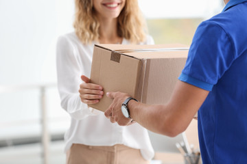 Young woman receiving parcel from courier indoors - obrazy, fototapety, plakaty