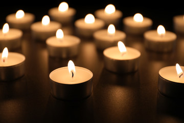 Fototapeta na wymiar Burning candles on table in darkness, closeup. Funeral symbol