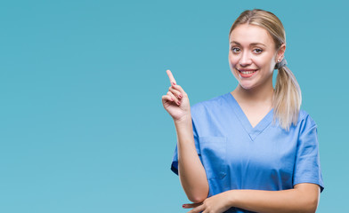 Young blonde surgeon doctor woman wearing medical uniform over isolated background with a big smile on face, pointing with hand and finger to the side looking at the camera.