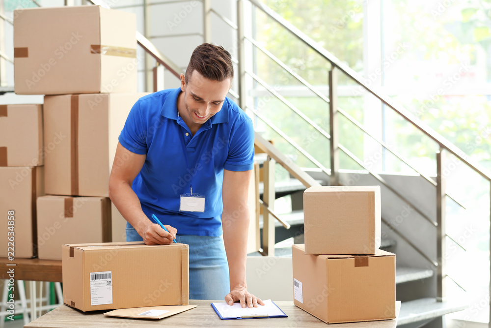 Sticker Young courier making notes on parcels at delivery department