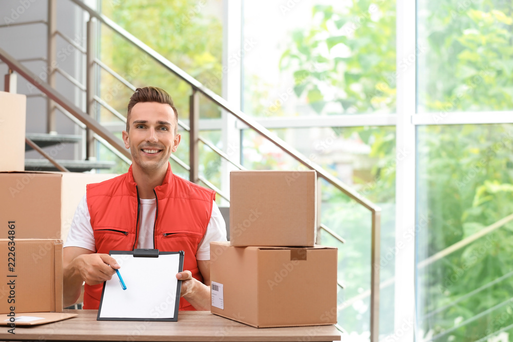 Poster Young courier with clipboard among parcels at delivery department. Space for text