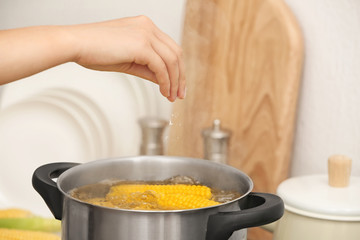 Woman salting water with corn cobs in stewpot, closeup