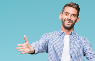 Young handsome man wearing white t-shirt over isolated background looking at the camera smiling with open arms for hug. Cheerful expression embracing happiness.