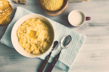 Wheat groats, millet porridge and melting butter in white bowl on kitchen table. Selective focus. Closeup. Copy space.