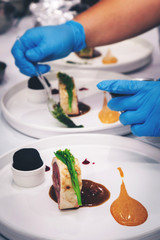chef is cooking lamb meat steak with mustard, red berry sauce and charcoal bread in hotel or restaurant kitchen. food stylist decorating dinner dish for customer.  selective focus and vintage photo.