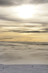Winter landscape with clouds below and beginning with the sunset