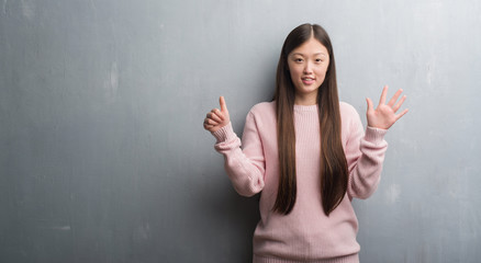 Young Chinese woman over grey wall showing and pointing up with fingers number six while smiling confident and happy.