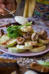 Woman hands adds toum garlic sauce paste, vegan mayonnaise with tea spoon to  backed, roasted assorted vegetables on plate. Healthy vegan lunch or vegetarian dinner. 