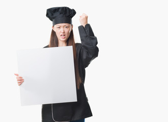 Young Chinese woman over isolated background wearing chef uniform holding banner annoyed and frustrated shouting with anger, crazy and yelling with raised hand, anger concept