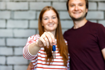 Young smiling couple showing keys to new home hugging looking at camera