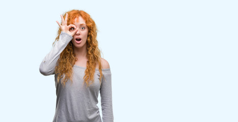 Young redhead woman doing ok gesture shocked with surprised face, eye looking through fingers. Unbelieving expression.