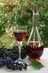 A bottle of red wine and a glass of wine on a white wooden table in the garden. Bunches of grapes. Picnic. Homemade