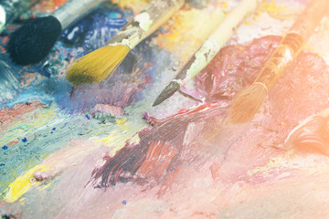 Paintbrushes closeup, artist palette and multicolor paint stains. Toned
