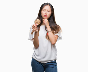 Young asian woman eating chocolate chip cookie over isolated background serious face thinking about question, very confused idea