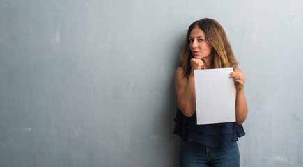 Middle age hispanic woman holding bank paper sheet serious face thinking about question, very confused idea