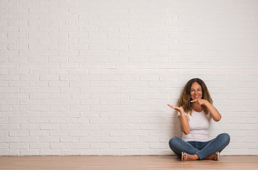 Middle age hispanic woman over white brick wall very happy pointing with hand and finger