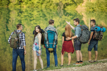 awesome beautiful girl is looking at the camera while her friends are admiring the beauty of nature during travelling. back view photo