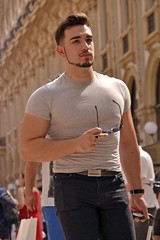 Young strong man walking pulling trolley on Milano travel background.