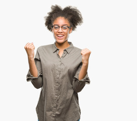 Young afro american woman wearing glasses over isolated background celebrating surprised and amazed for success with arms raised and open eyes. Winner concept.